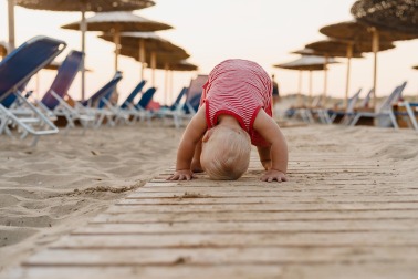 Smiling baby crawling and playing on seaside. Happy little child playing on beach near ocean. Babyhotel
